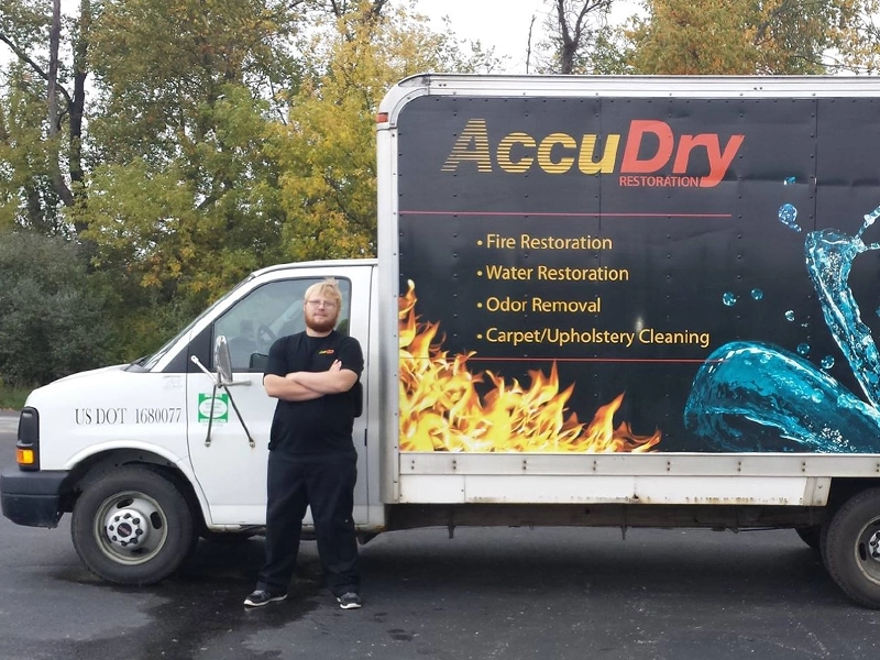 Man standing with arms crossed in front of a white restoration service truck with fire and water graphics.
