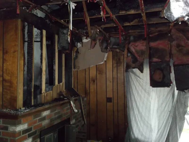 Fire-damaged room with exposed charred ceiling beams and partially burnt wooden walls.