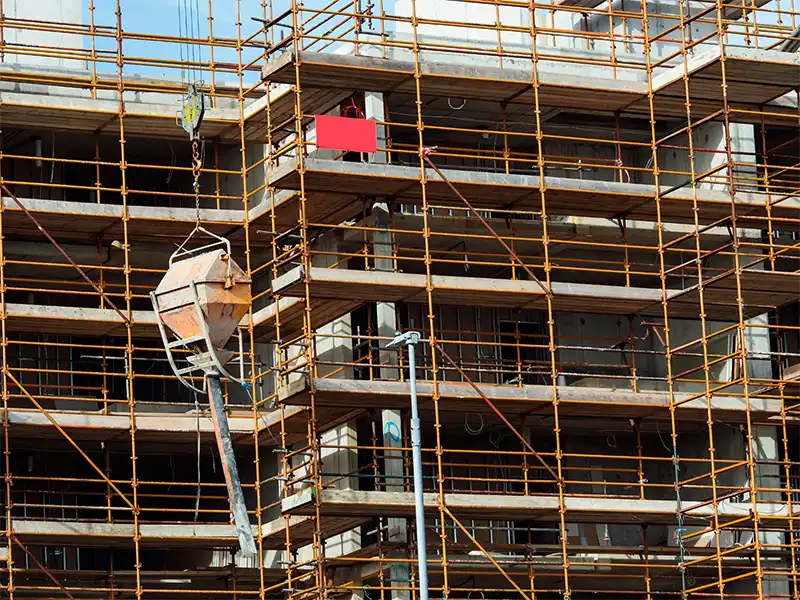 Scaffolding surrounding a multi-story building under construction with a suspended concrete bucket.