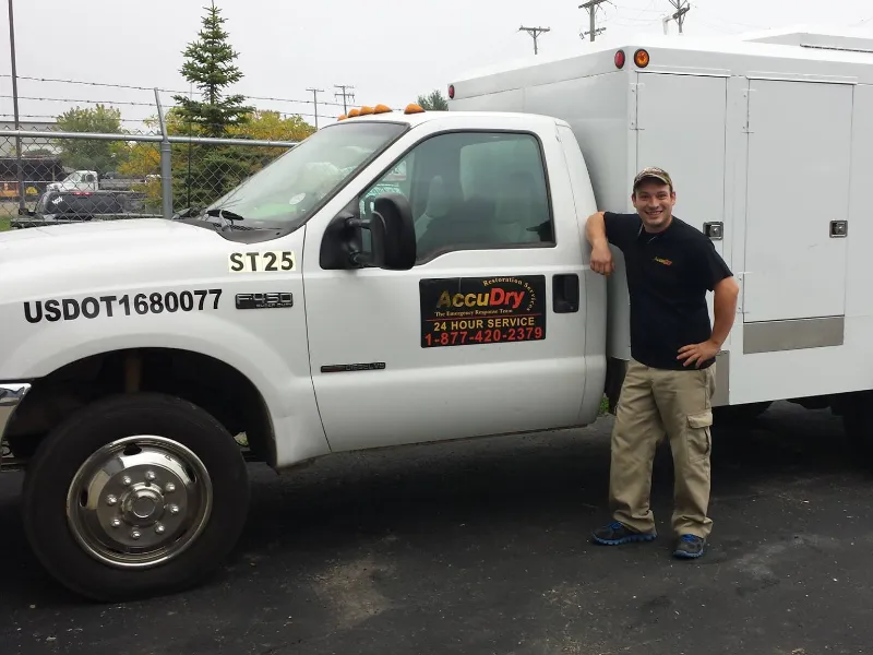 Man in work clothes leaning on a white service truck with AccuDry signage.