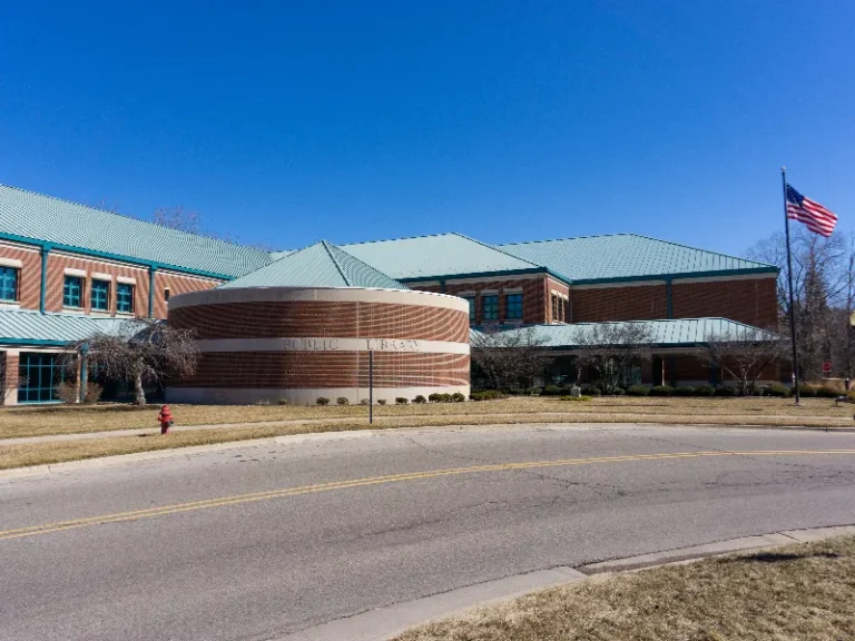 Public library building with a circular brick section, green roofs, and an American flag on a pole.